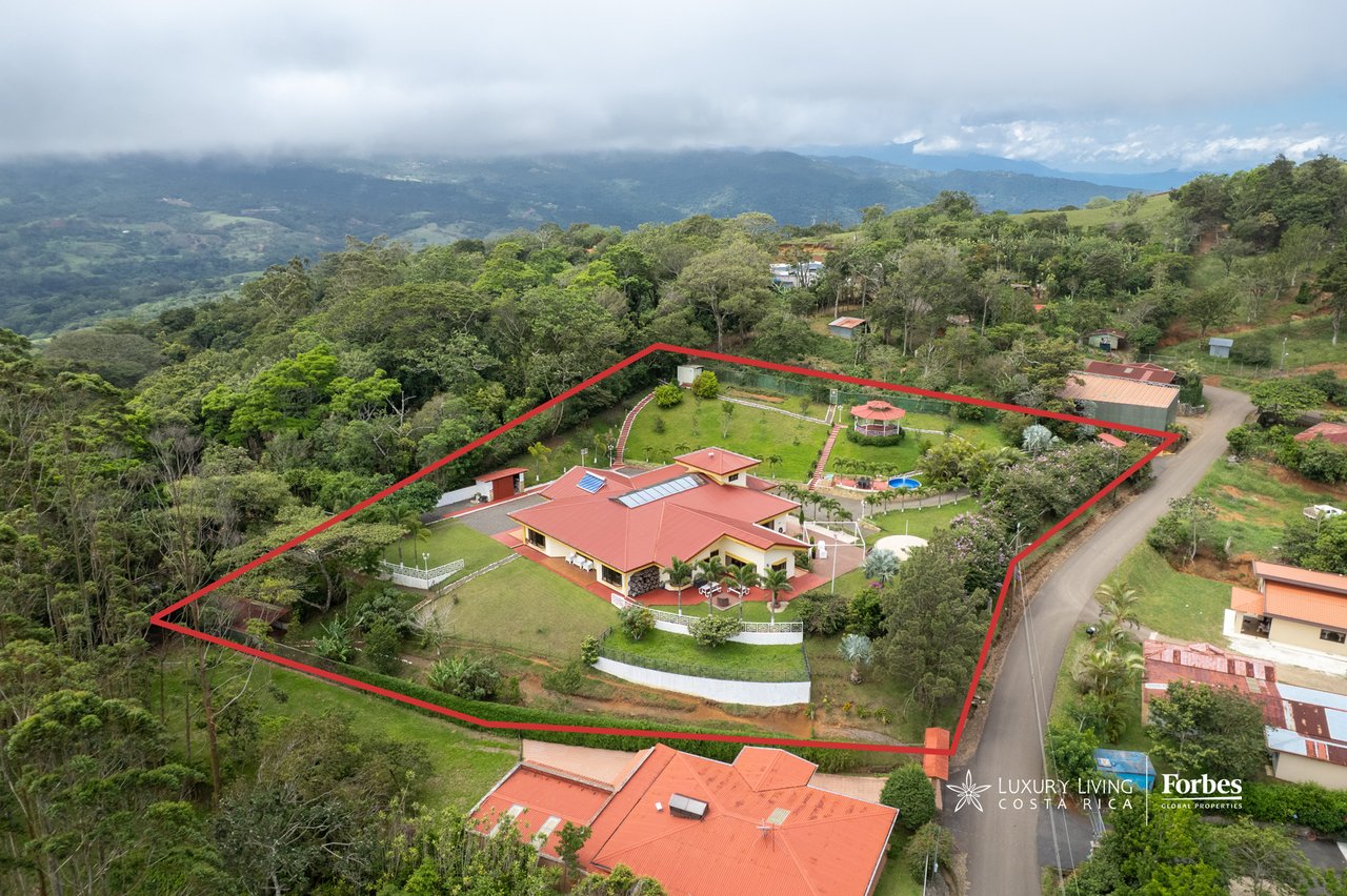 Aerial view of a red-roofed mountain house and grounds outlined in red, with a pool and forested mountains beyond.
