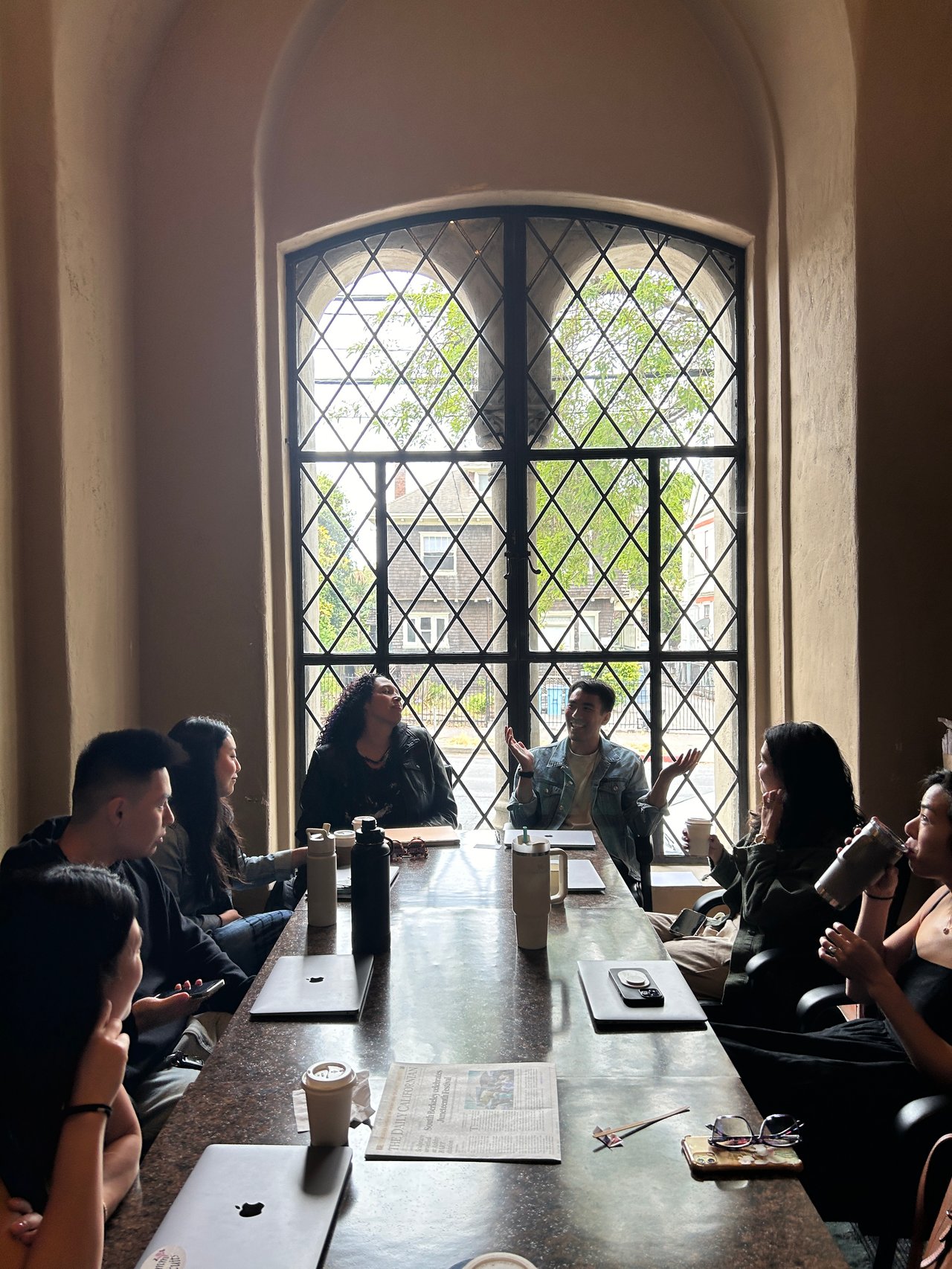 A group meeting around a long table beneath a tall arched window.