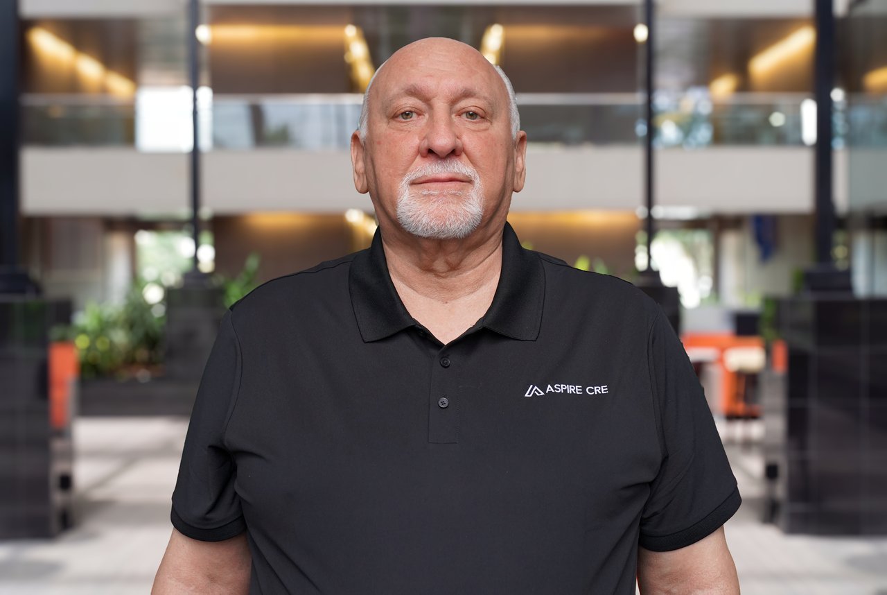 Ralph Mangus in a black Aspire CRE polo in a modern office lobby.