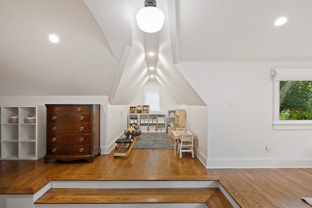 Playroom with a vaulted ceiling, hardwood steps, and children’s toys and furniture.