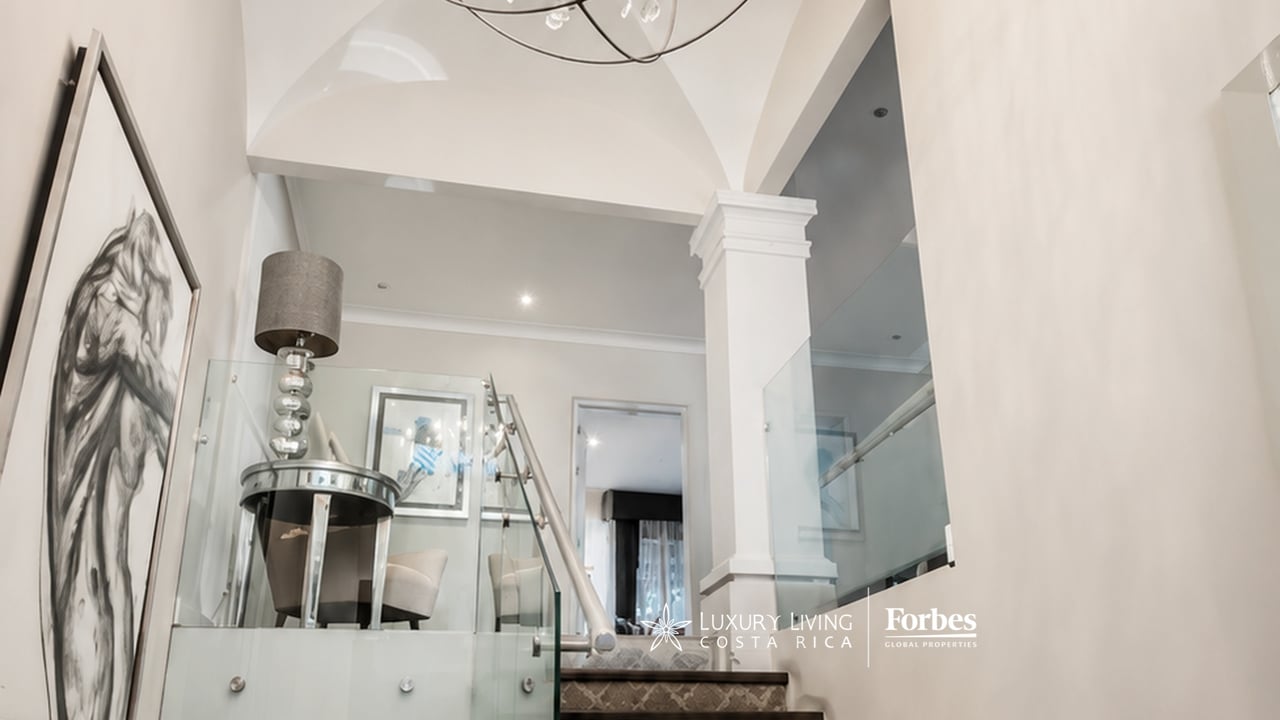 Home staircase with glass railings, a console table, framed artwork, and a high vaulted ceiling.