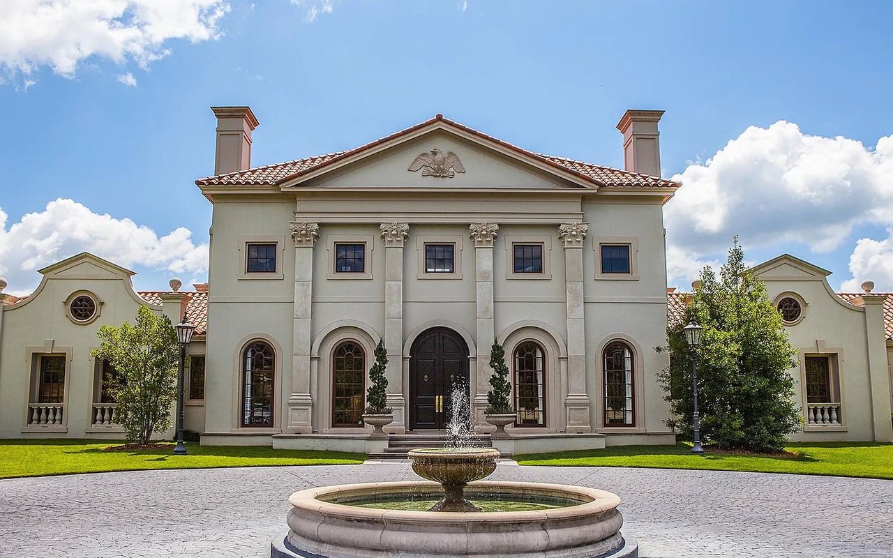Classical cream estate with columns and a fountain in the front drive.