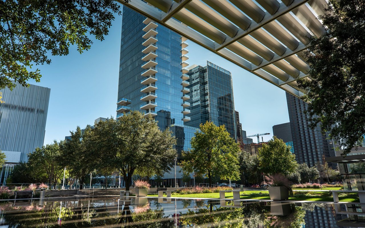 Downtown Dallas high-rises rise above a landscaped plaza and reflective pool.