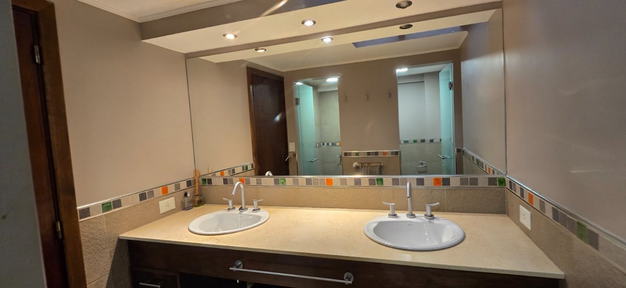 Bathroom vanity with two sinks, a large mirror, and a multicolored tile border.