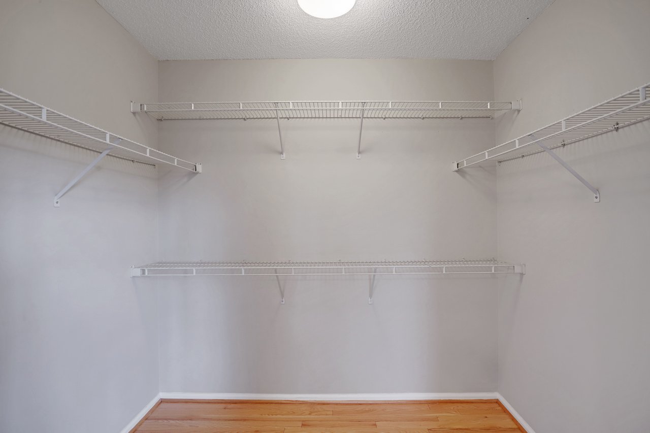 Empty walk-in closet with white wire shelves on three walls and hardwood flooring.