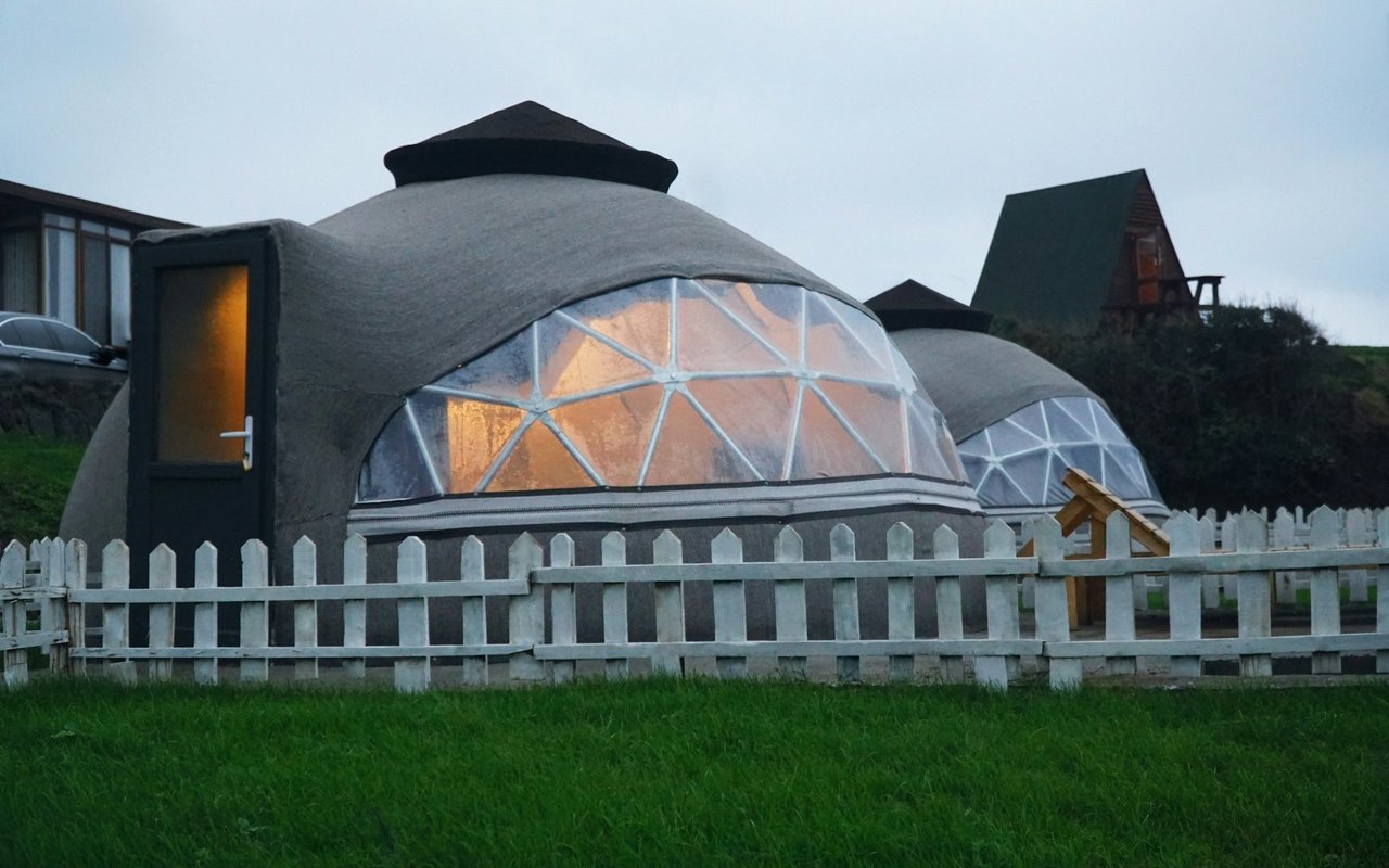 Dome-shaped homes with translucent window panels glow behind a white picket fence.
