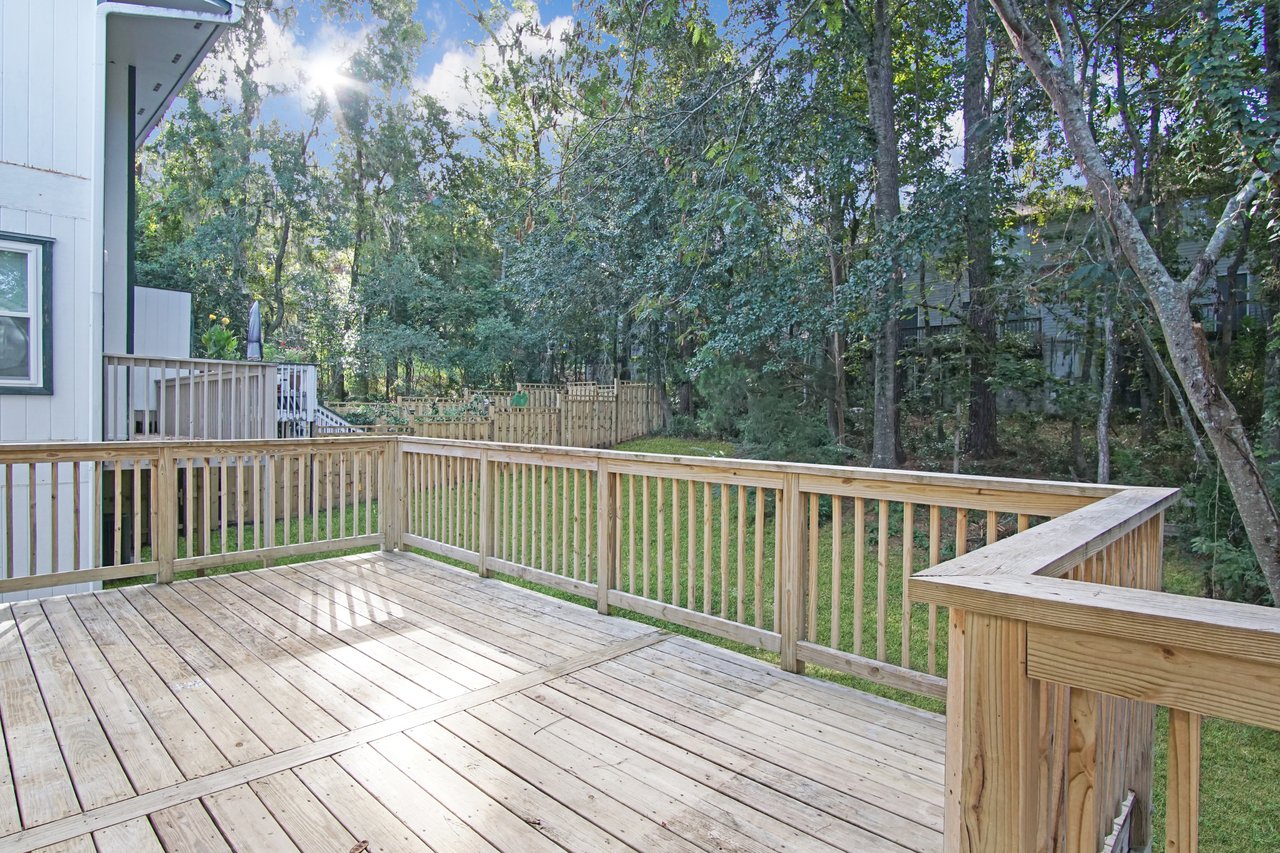 Back deck of the townhome at 529 Collinsford Road, Tallahassee, Florida, featuring a spacious wooden deck with railings overlooking a fenced backyard and shaded by tall trees. The area offers a peaceful outdoor retreat with views of natural greenery.