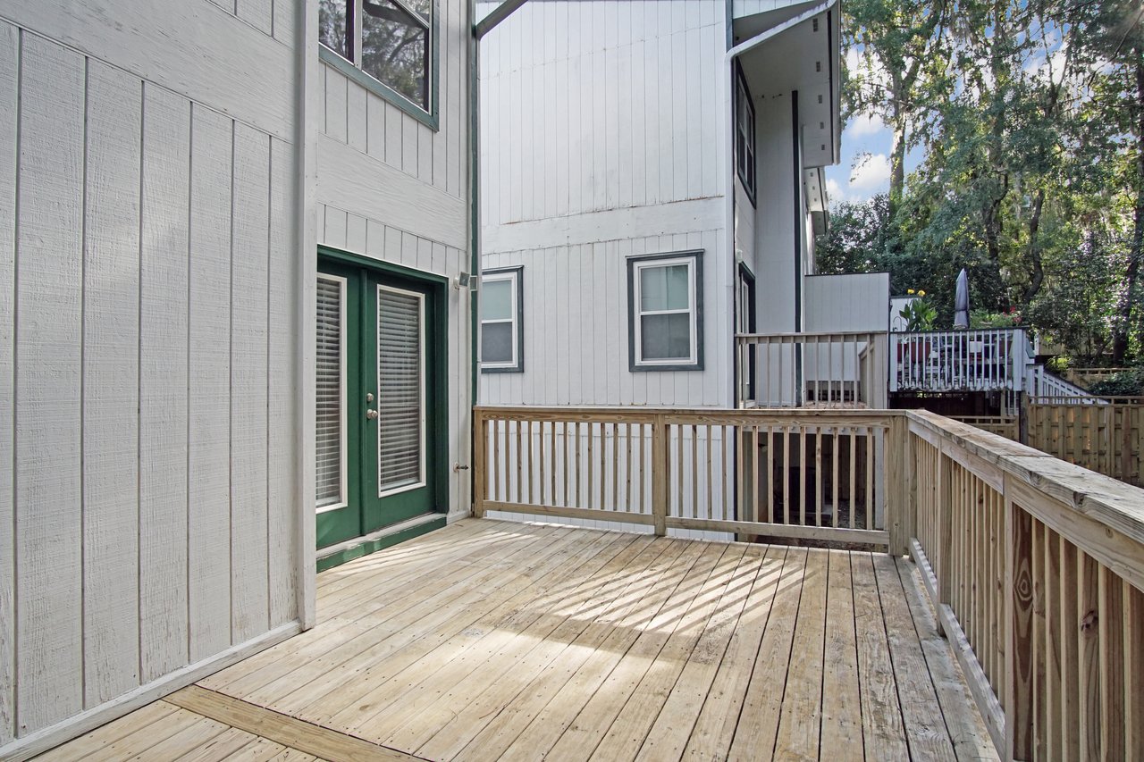 Back deck of the townhome at 529 Collinsford Road, Tallahassee, Florida, featuring a spacious wooden deck with railing and French doors framed in green trim leading into the home. The area offers an ideal outdoor space for seating or entertaining, and shaded by mature trees.