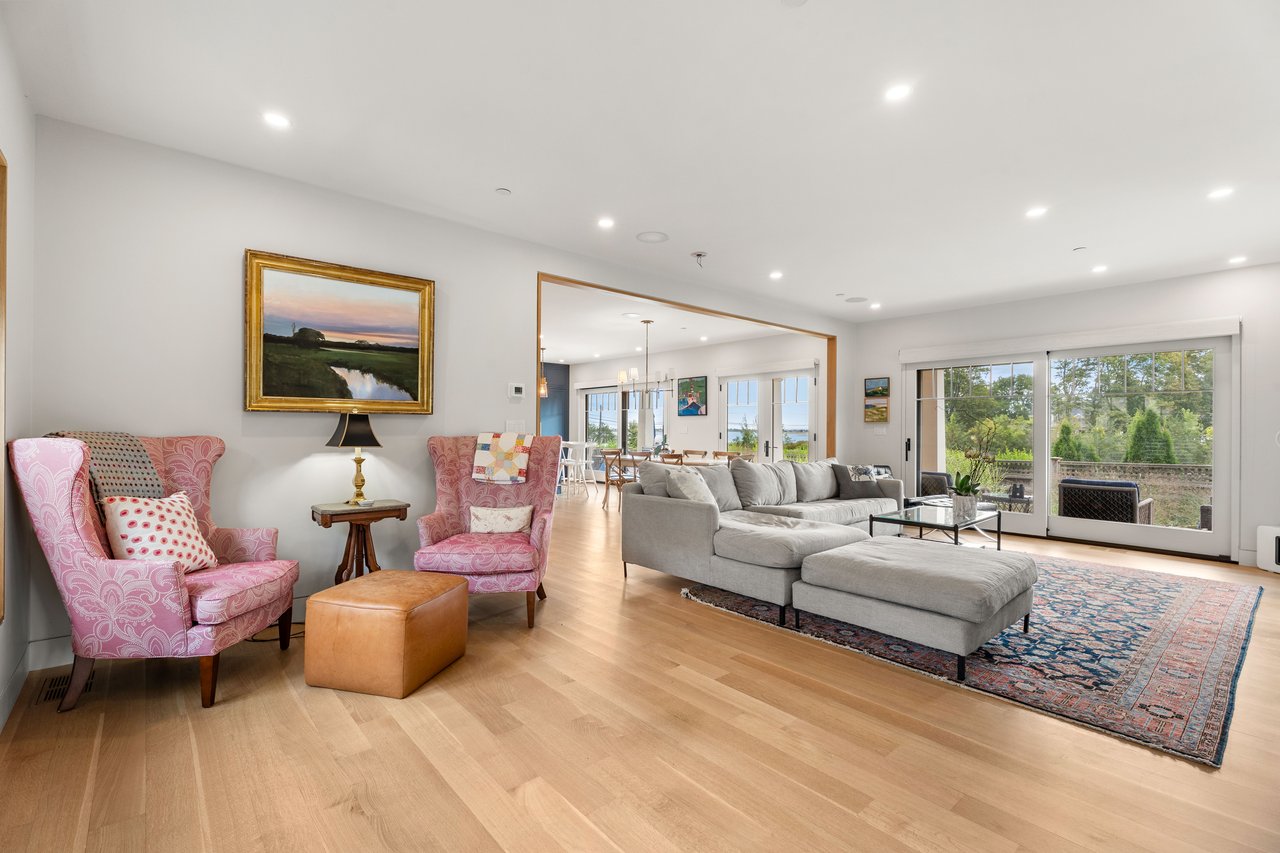 Open-plan living room with pink armchairs, a gray sectional, and sliding doors overlooking a deck and garden.