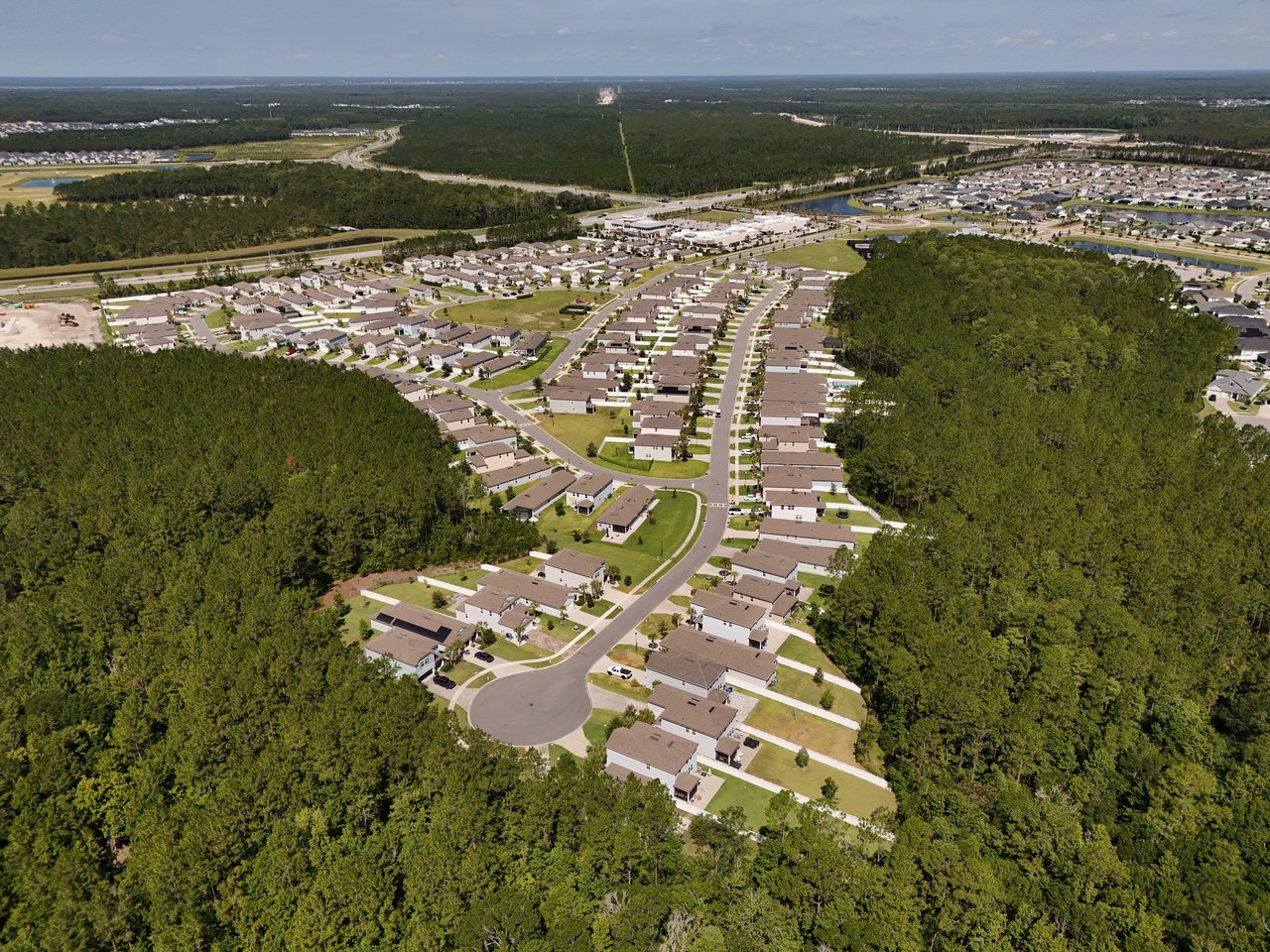 Aerial view of homes along curving streets, surrounded by dense woodland.