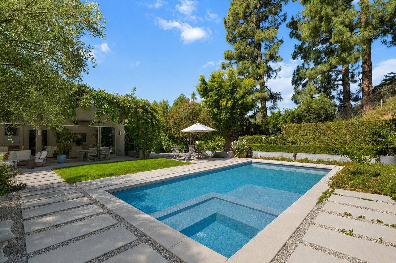 Backyard swimming pool with a shallow ledge, stone patio, and landscaped seating area.