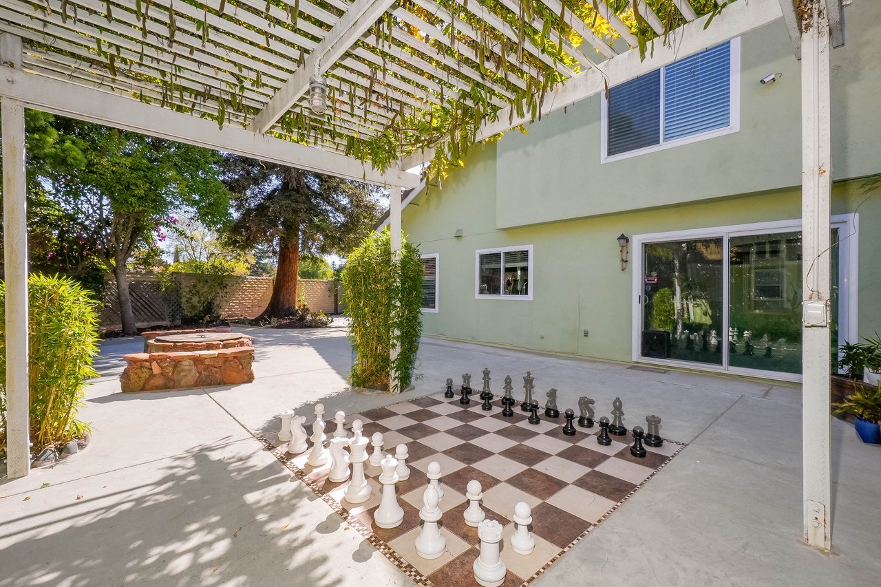 Backyard patio with a pergola, oversized chess set, and stone fire pit.