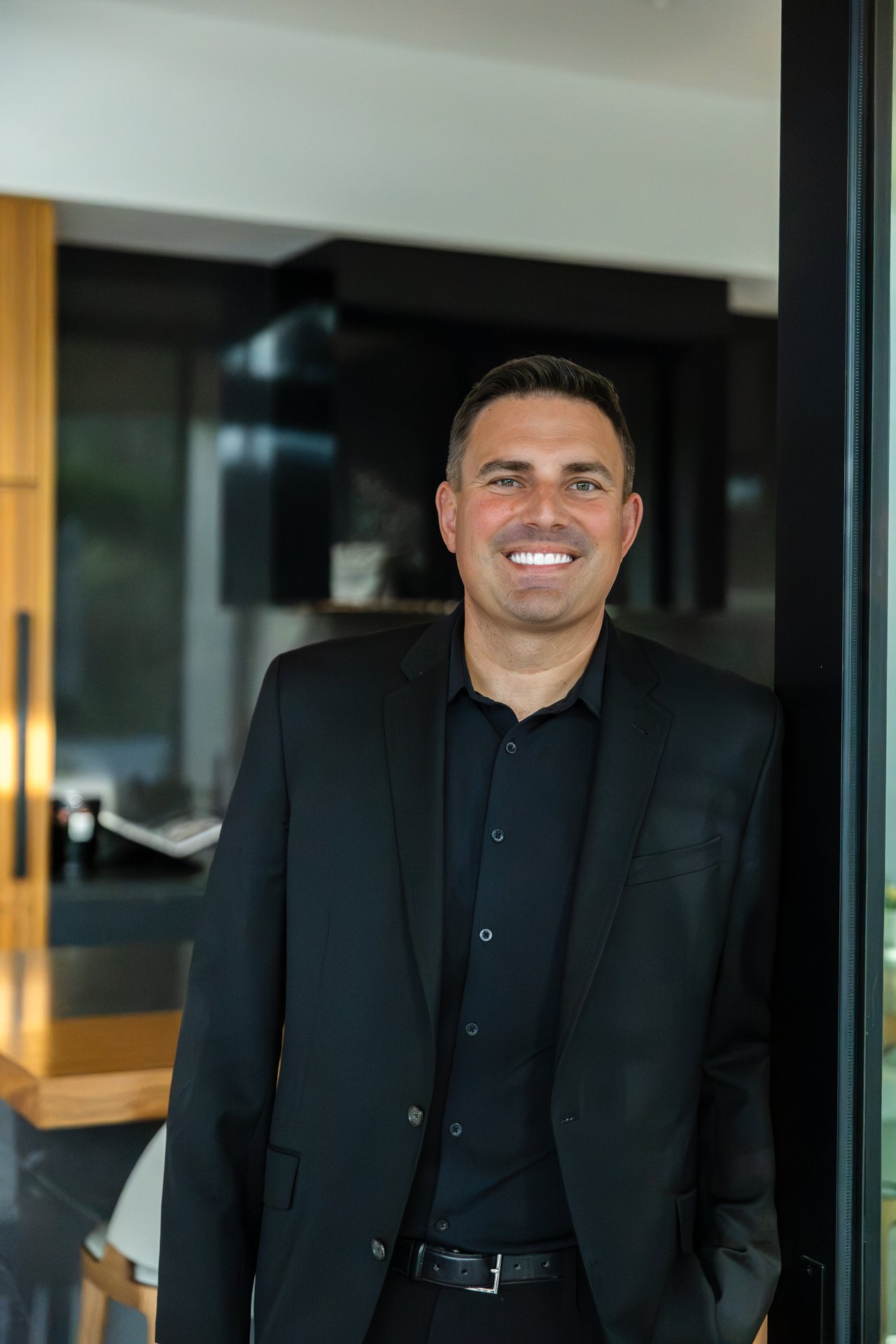 Brent Votroubek smiling in a black suit inside a modern interior.