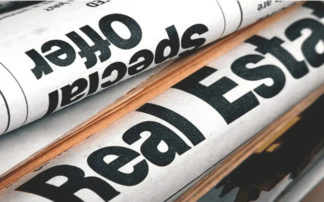 Rolled newspapers with “Real Estate” printed prominently across the foreground.