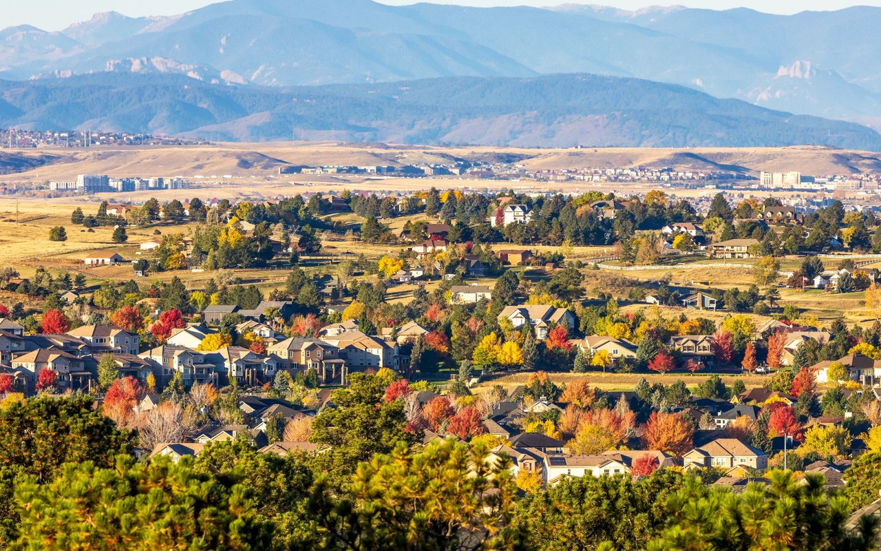 Suburban homes and colorful autumn trees below a broad mountain range.