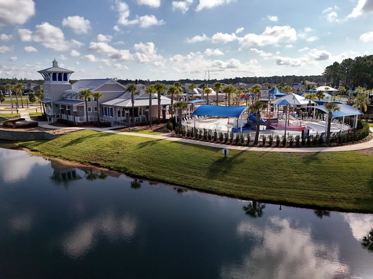 Community clubhouse and pool complex with blue shade canopies beside a pond.