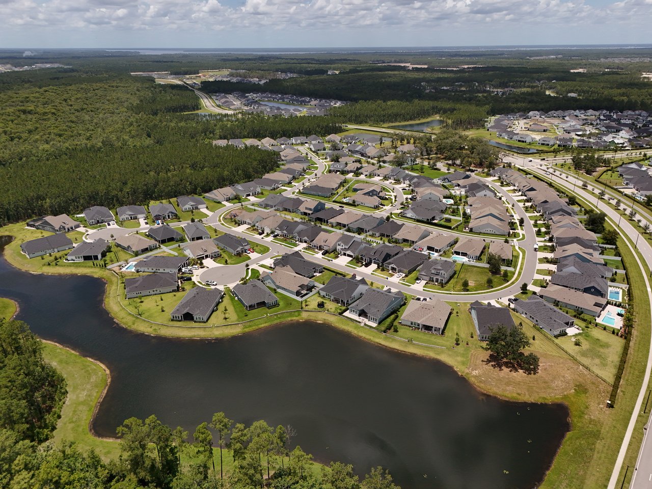 Aerial view of homes around a large pond, with wooded areas beyond the neighborhood.