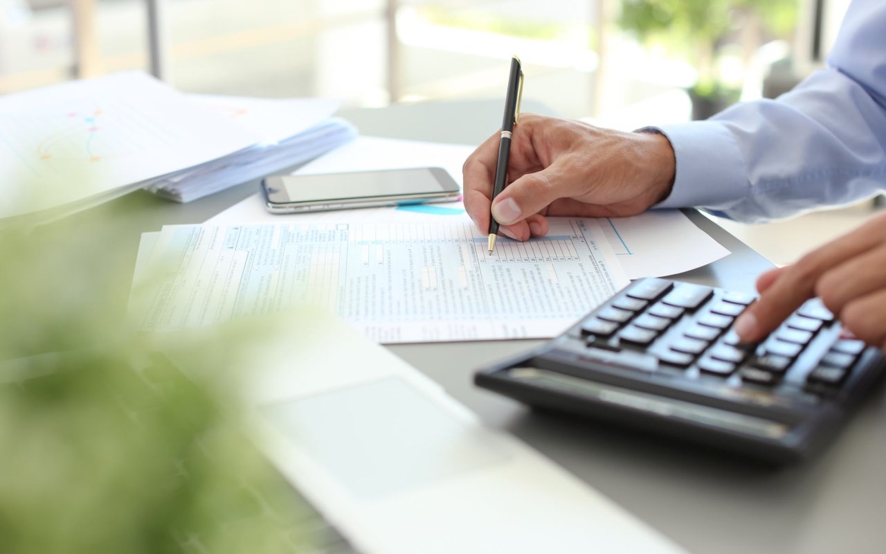 A person fills out financial paperwork beside a smartphone and calculator.