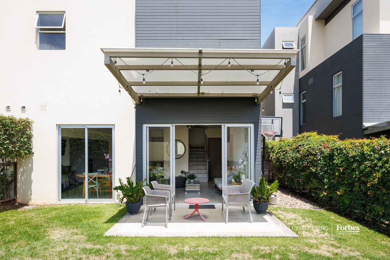 Townhouse rear patio with outdoor seating beneath a covered pergola, opening onto a lawn.
