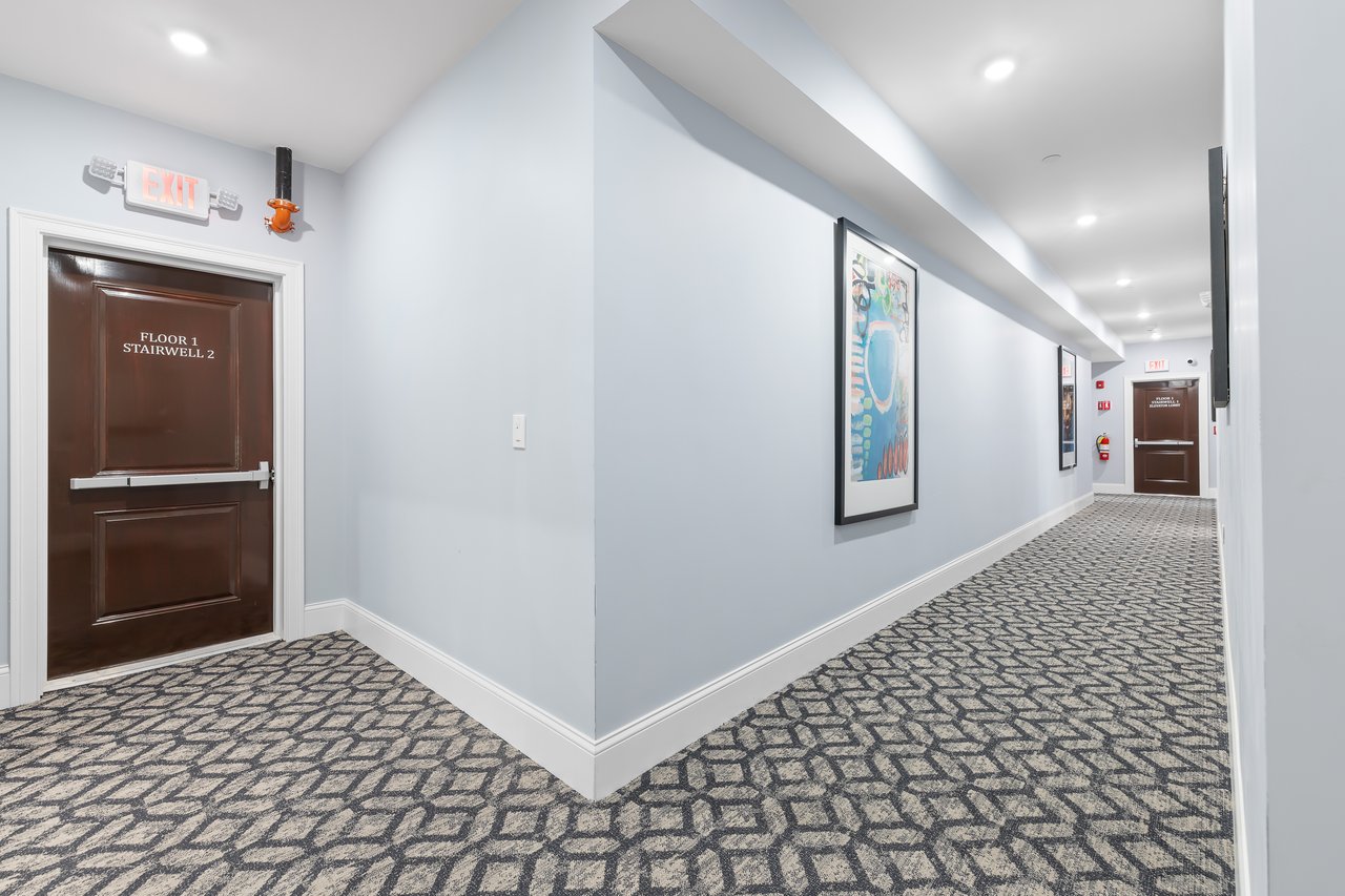 Hallway with patterned carpet, framed artwork, and a brown door marked Floor 1 Stairwell 2.