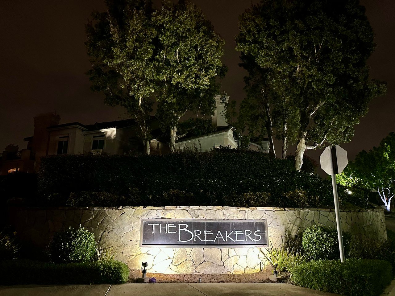 The Breakers sub-community entry in Bear Brand, Laguna Niguel — illuminated stone wall with Mediterranean townhomes in background