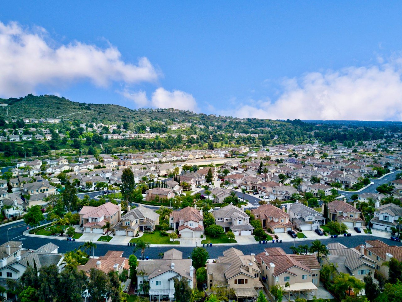 Aerial view of a suburban neighborhood below a green hillside.