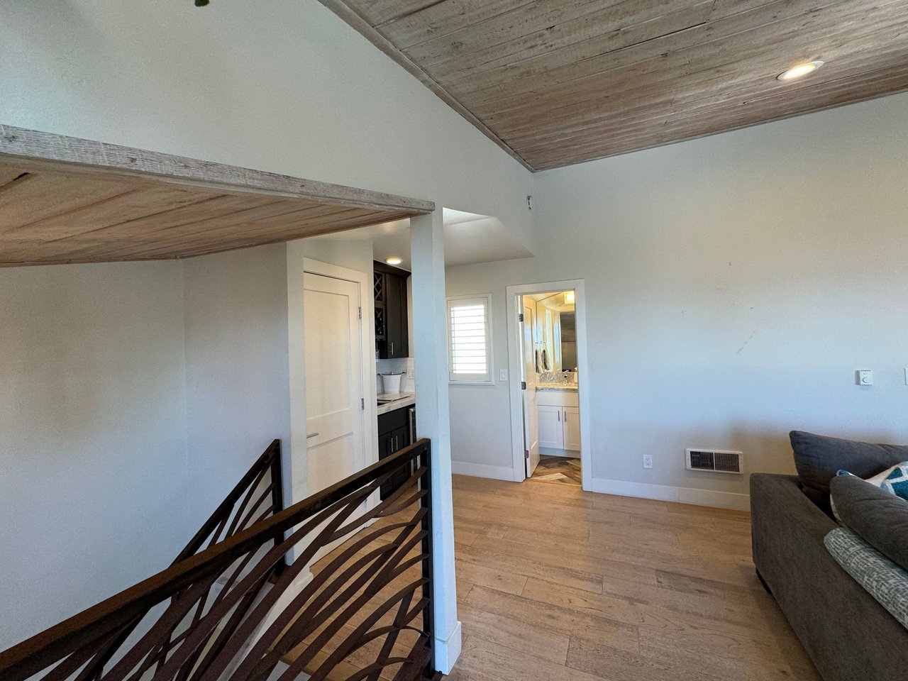 Interior view of hallway with modern railing, wood flooring, and entry to kitchen and bathroom at 533 S Sierra Ave, Solana Beach, CA 92075 oceanview rental.