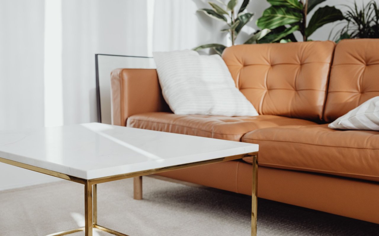 Living room with a cognac tufted leather sofa and a white marble coffee table with gold legs.
