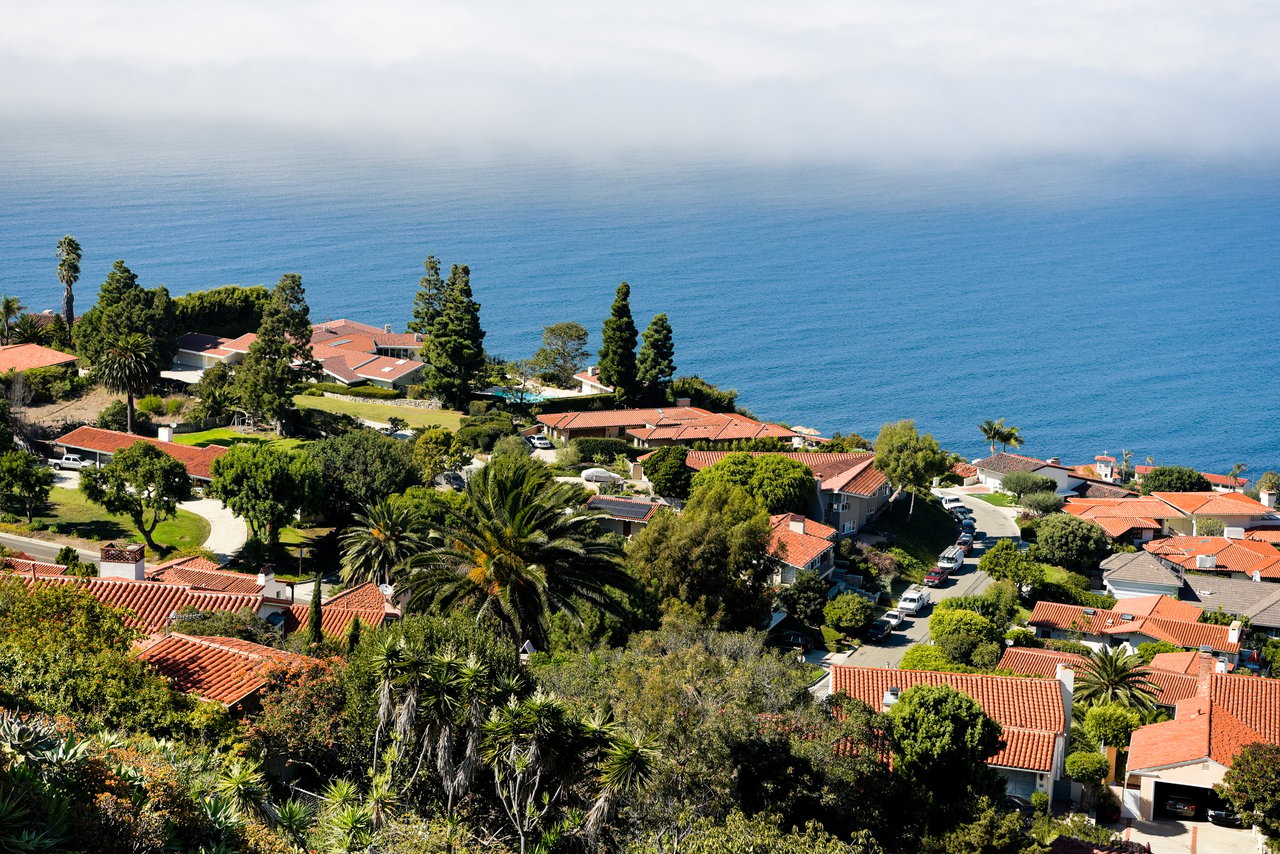 Coastal neighborhood of red-tile-roof homes overlooking the ocean.