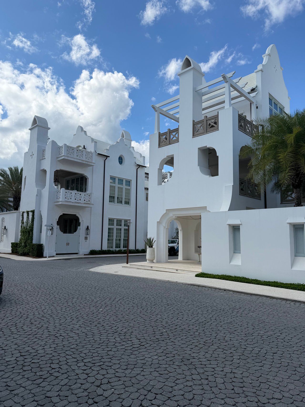 Stunning white Moorish-style luxury homes with dark wood balconies along a cobblestone street in Alys Beach.
