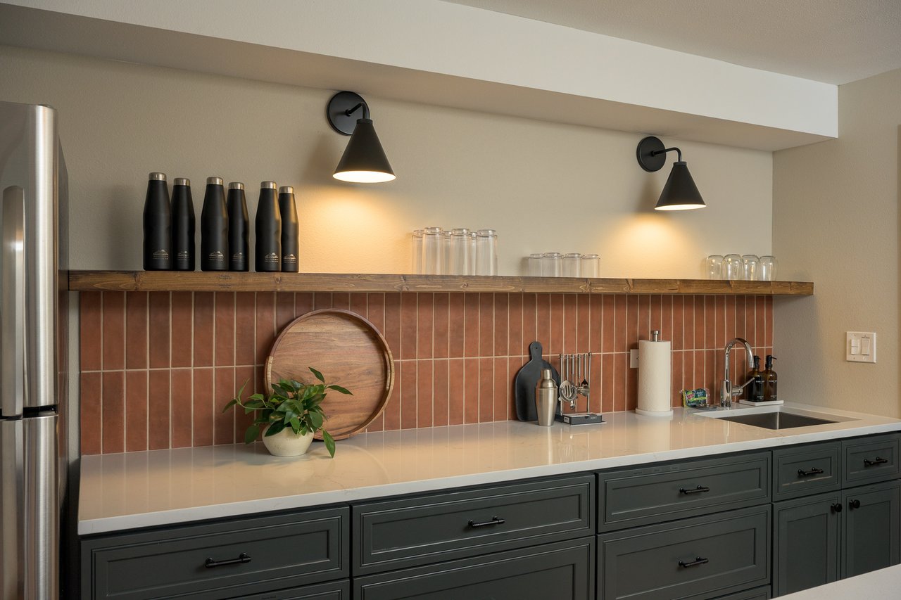 Kitchen with dark green cabinets, terracotta tile backsplash, and a long wood shelf.