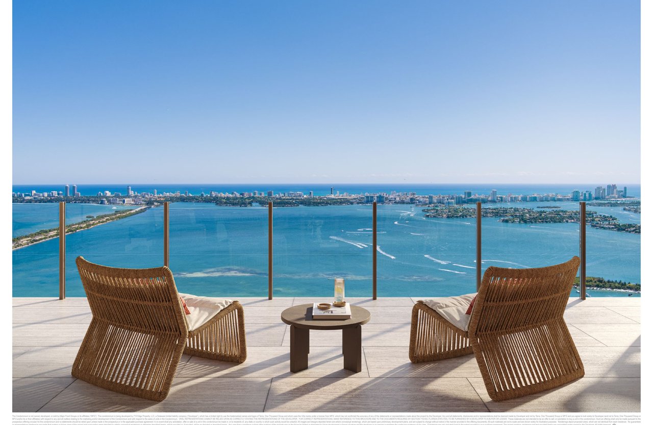 Furnished balcony overlooking Biscayne Bay and the Miami skyline, with woven lounge chairs beside a glass railing.