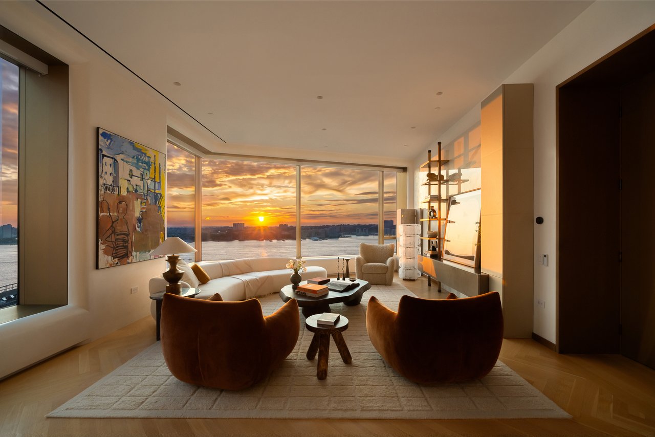 Furnished living room with floor-to-ceiling windows overlooking the water at sunset.