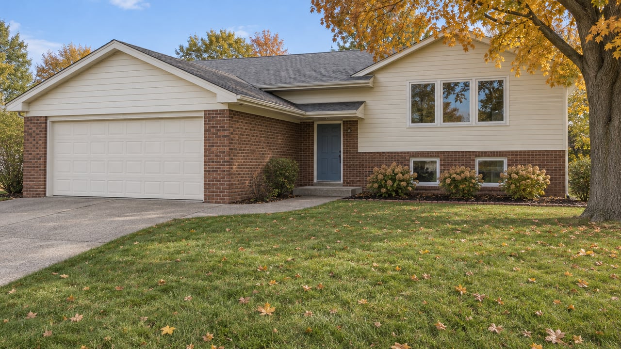Split-level house with cream siding, brick lower walls and an offset blue entry beyond an autumn lawn and concrete approach.