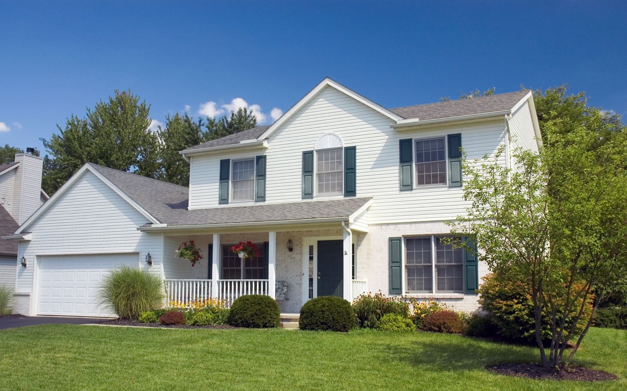 Two-story white house with green shutters, attached garage, covered porch, and landscaped front lawn.