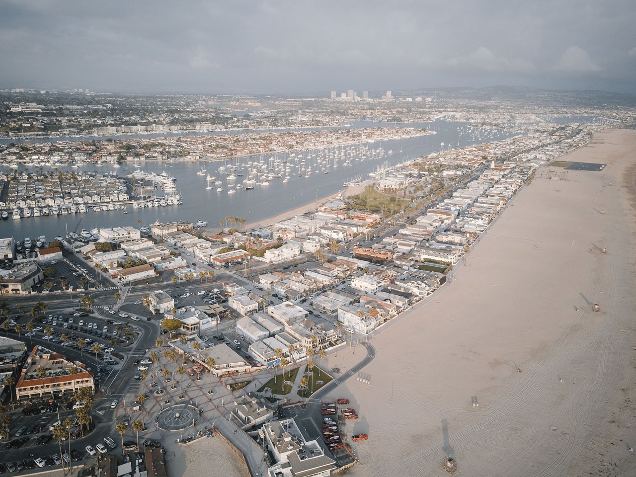 Aerial view of Newport Beach harbor, sailboats, coastal homes, and sandy beach.
