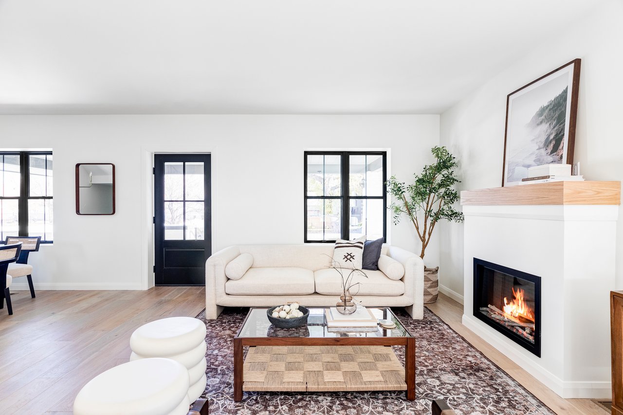 Bright living room with white couch, coffee table, large front-facing windows and has fireplace