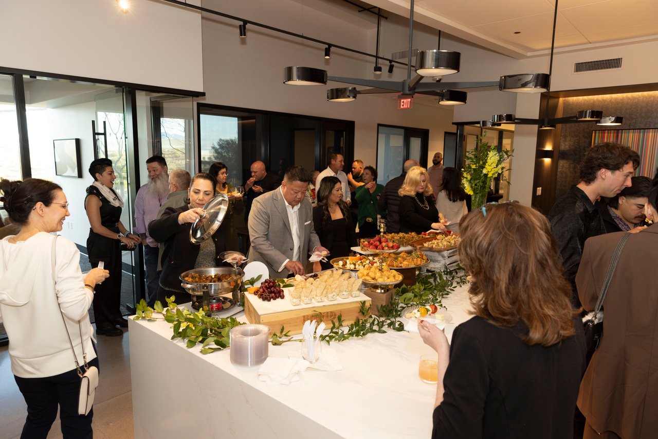 Guests mingle around a buffet at a client appreciation open house in a modern event space.
