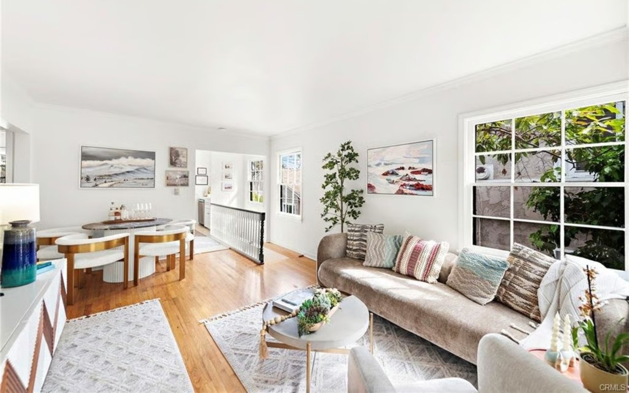 Living and dining room with hardwood floors, a neutral sofa, and large windows.