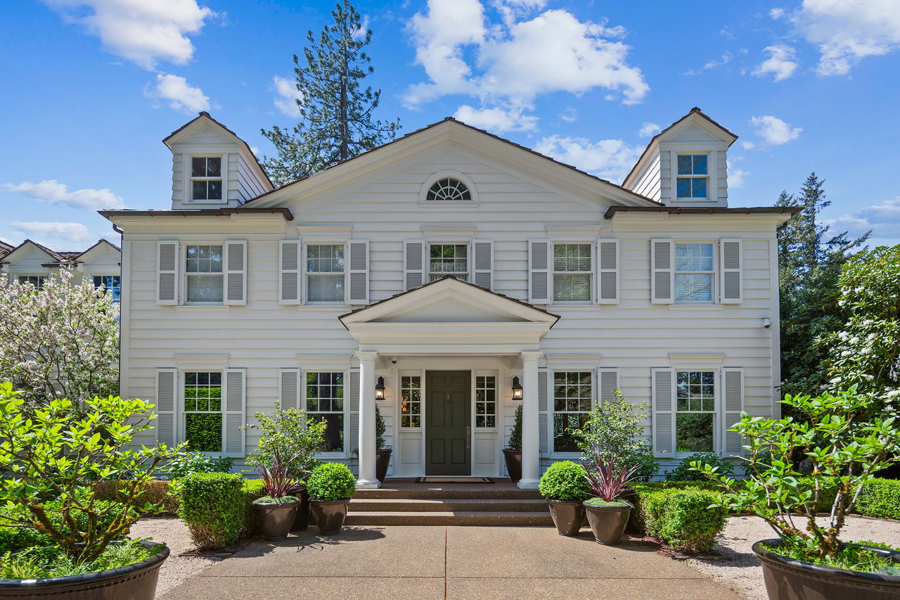 White two-story house with twin dormers, gray shutters, and a landscaped front entrance.