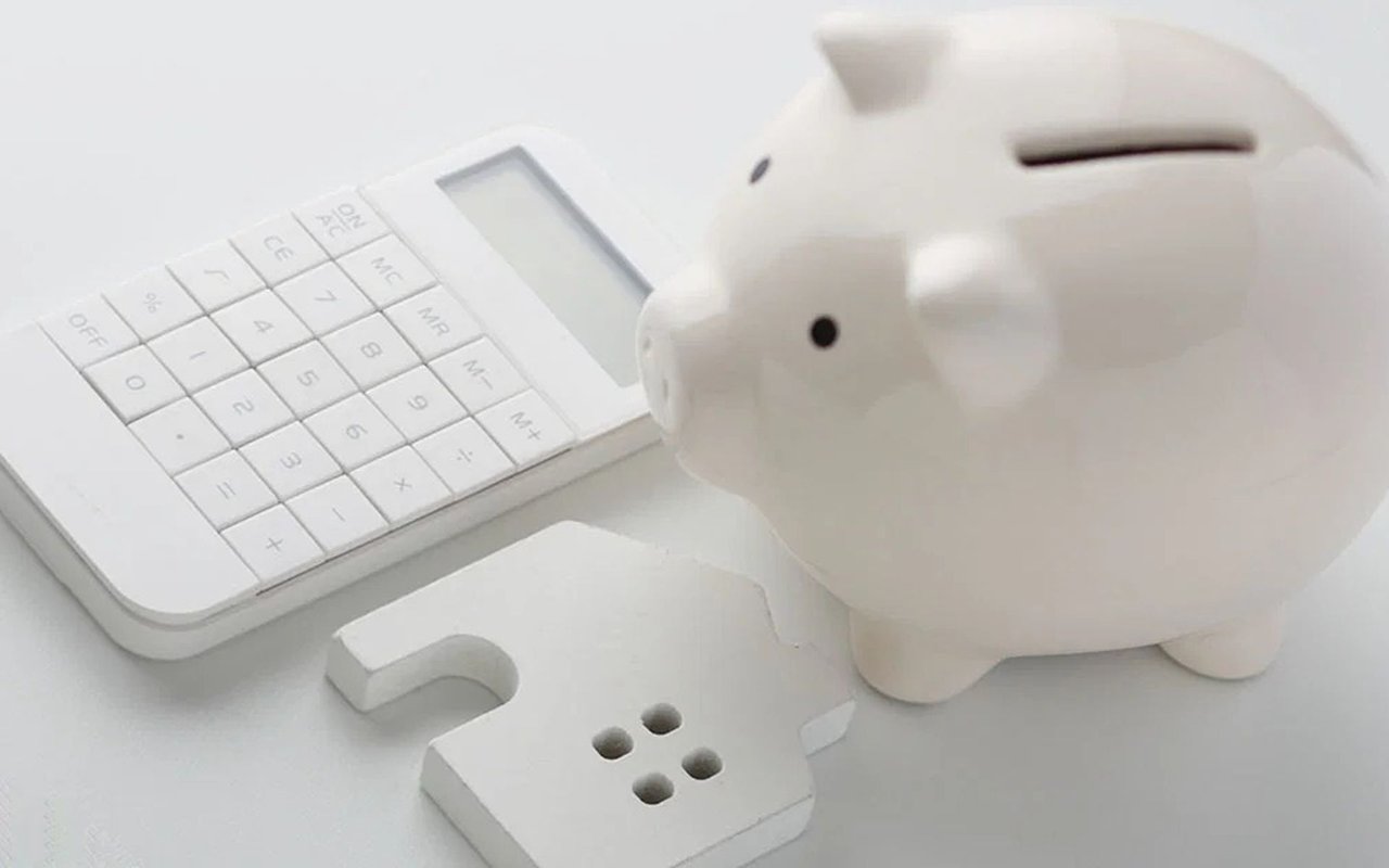 White piggy bank beside a calculator and a house-shaped key.