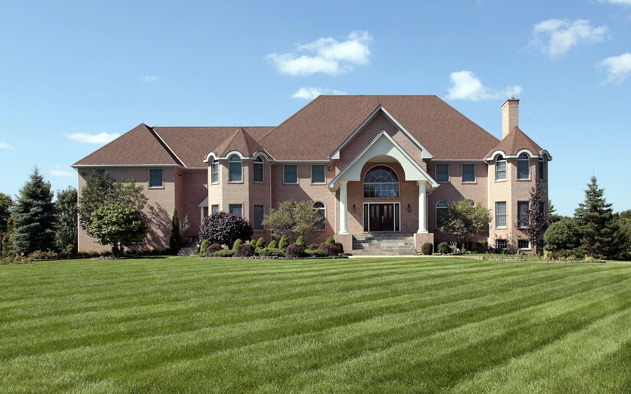 Large brick house with a central arched entrance, landscaped shrubs, and a freshly mowed lawn.