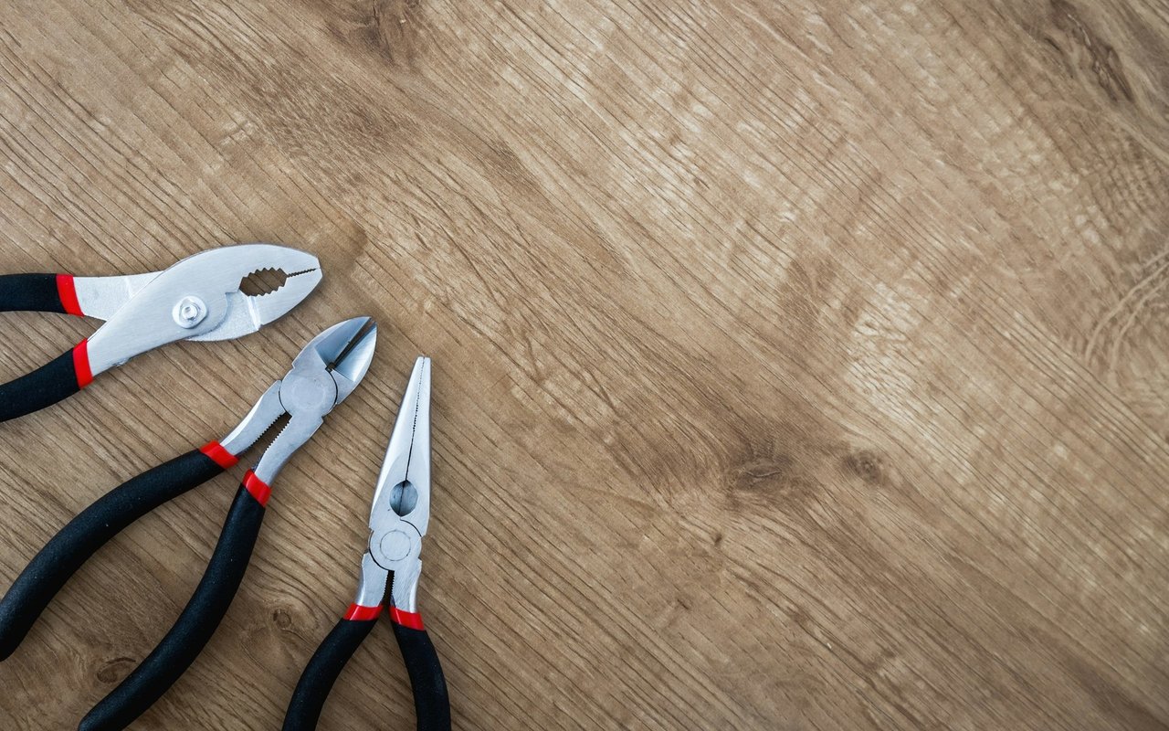 Three pliers with black and red handles on a wooden work surface.