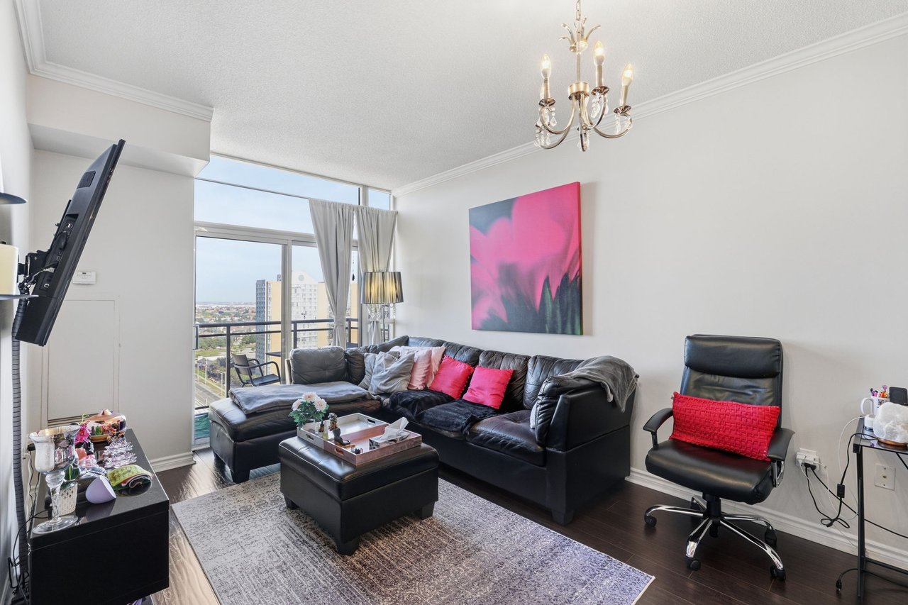 Penthouse living room with a black leather sectional, pink artwork, and large windows overlooking Mississauga.