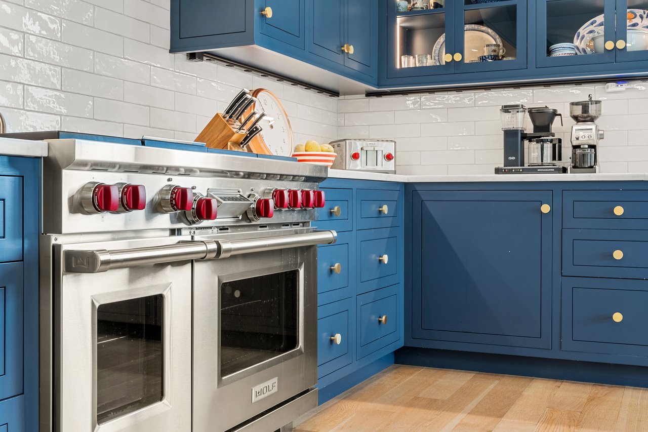 Kitchen with deep blue cabinets, brass knobs, and a stainless steel range with red controls.