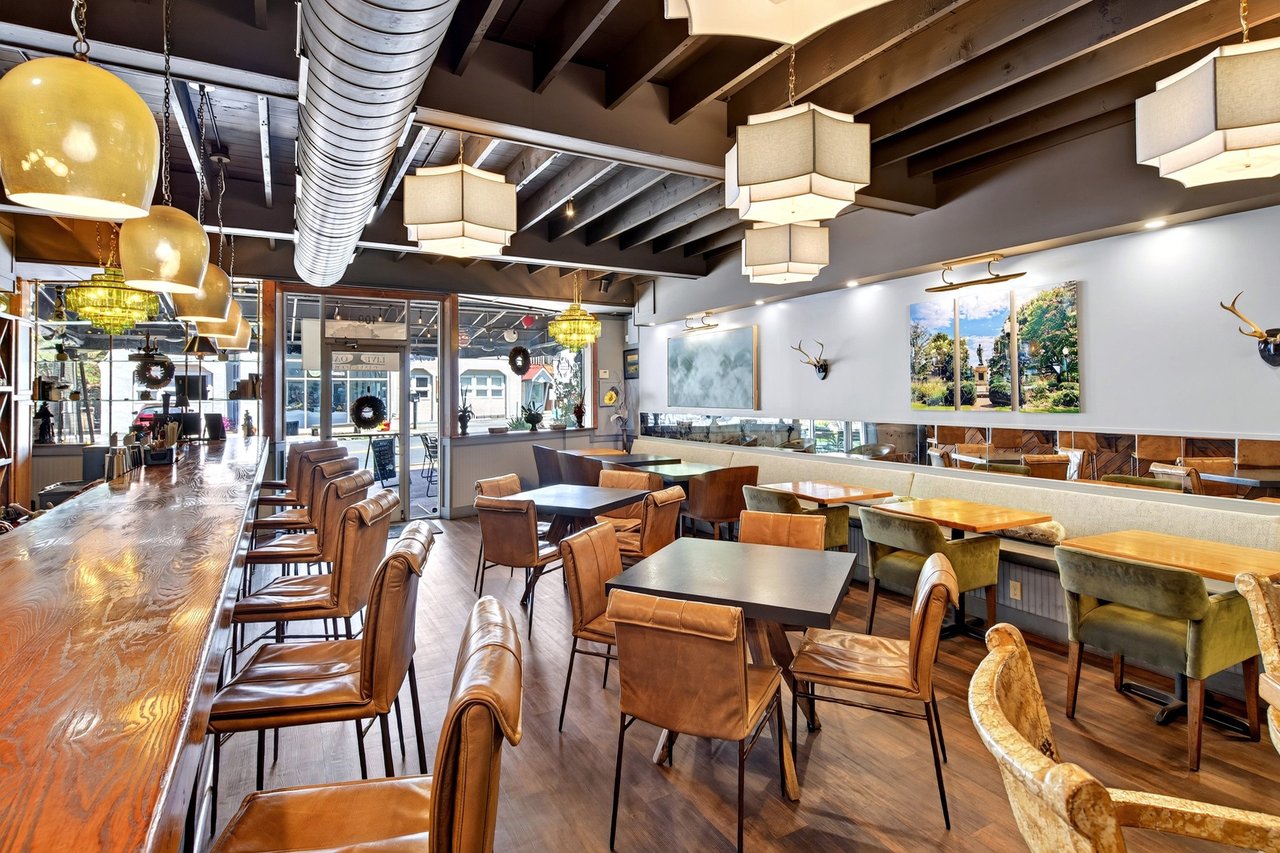 Restaurant dining room with leather seating, a long wood bar, and exposed ceiling beams.