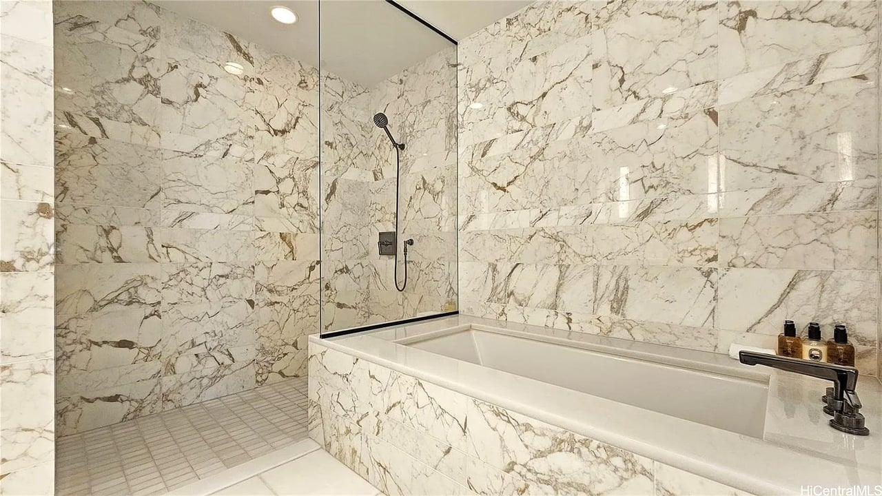Marble bathroom with a glass-enclosed shower and a white bathtub.