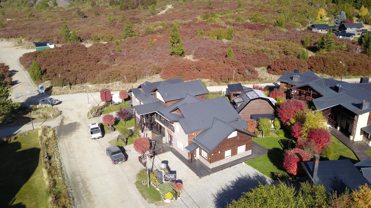 Aerial view of chalet-style buildings among autumn trees beside a gravel drive.
