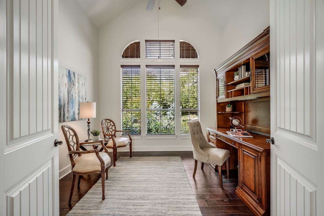 Furnished home office with a dark wood built-in desk and tall shuttered windows.