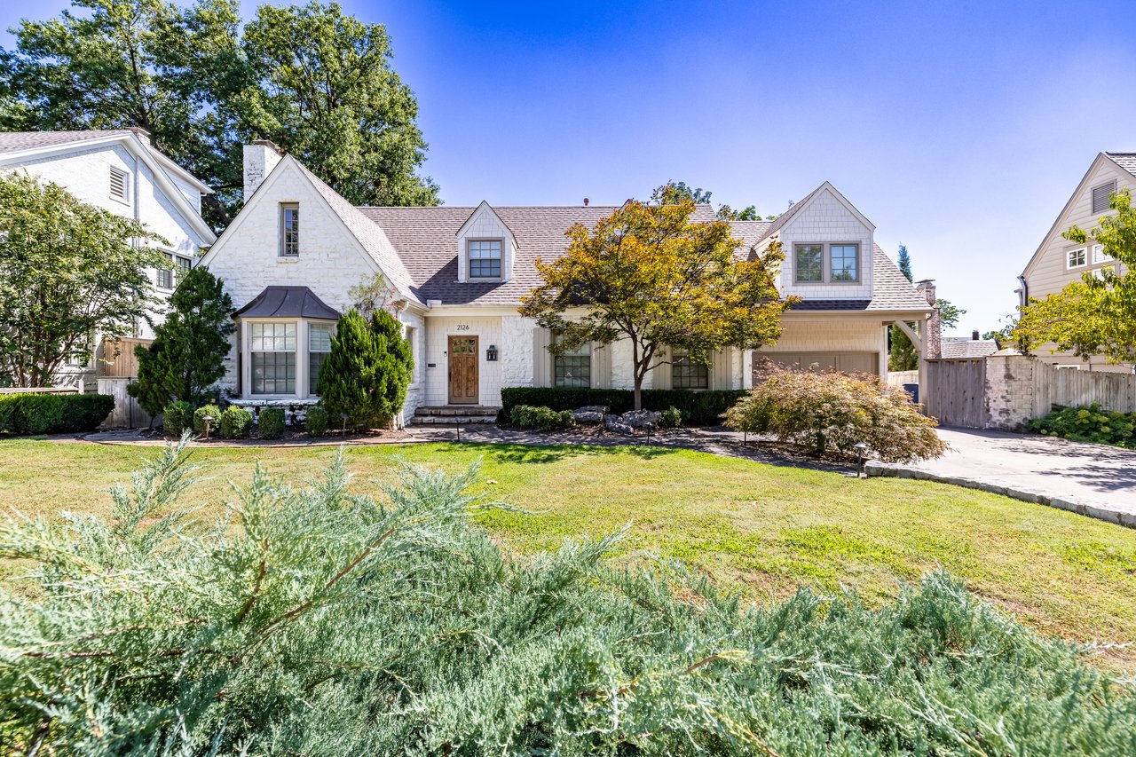 White stone house with multiple gables, an attached garage, and a landscaped front lawn.